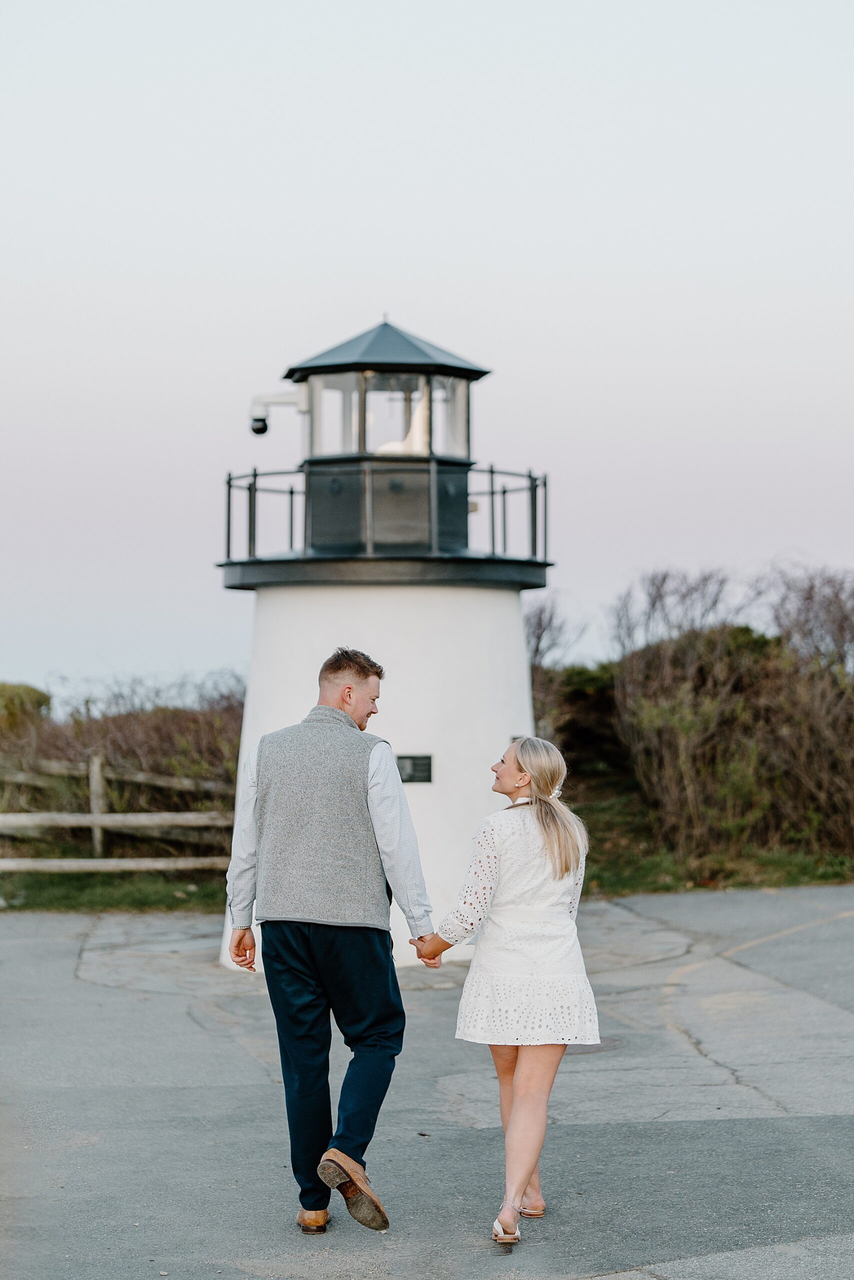 couple hold hands and walk towards lighthouse