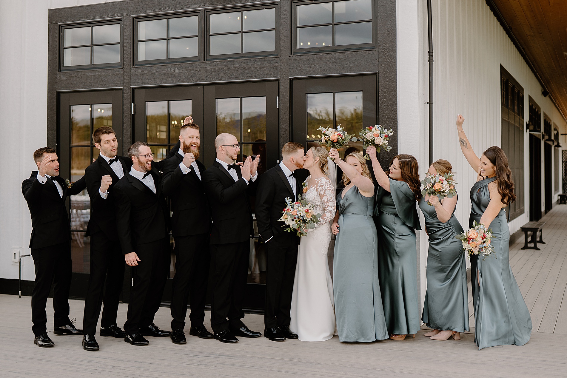 wedding party cheers as bride and groom kiss