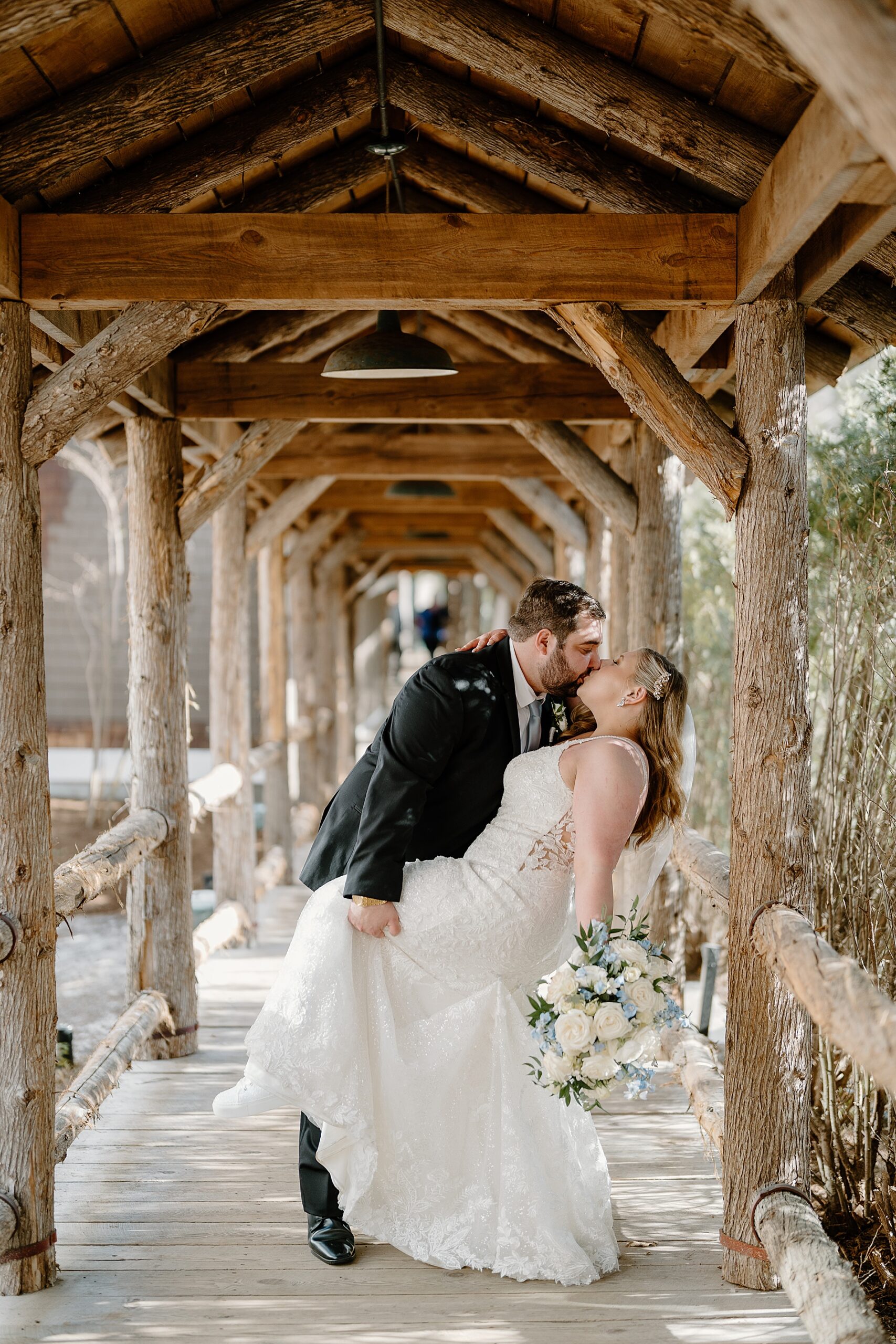 bride and groom kiss on covered bridge at Church Landing Wedding at Mill Falls at the Lake  